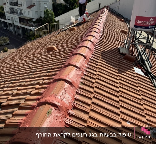 אדם עומד על גג רעפים עם חומר איטום אדום